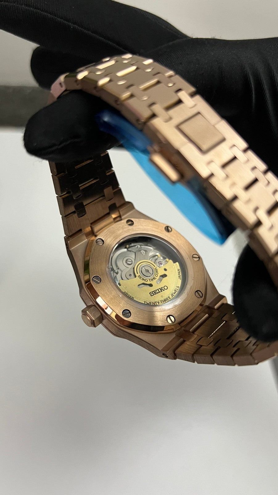 Royal Oak (Rose Gold) Seiko NH35 automatic mod watch. A caseback detail shows the exposed mechanical movement of the rose gold watch held by a gloved hand.