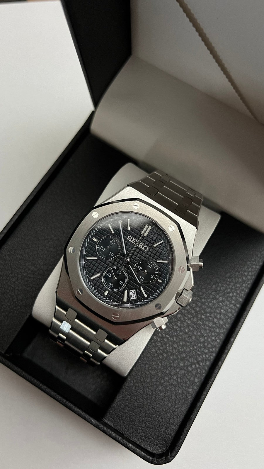 Royal Oak Chrono (Black) Seiko VK63 meca-quartz chronograph mod watch. A slightly angled shot of a silver chronograph watch with a black textured dial in a black display box.