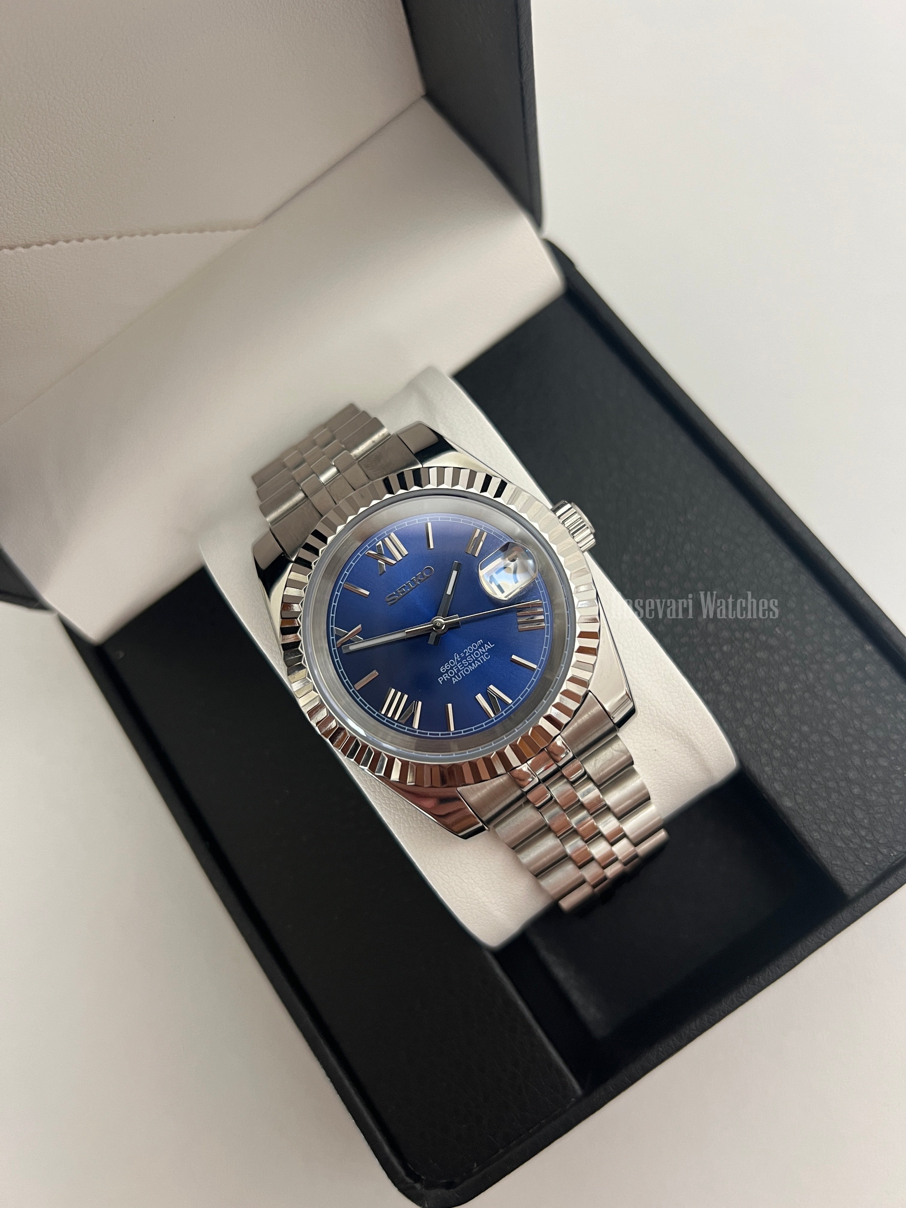 Datejust (Royal Blue Roman) Seiko NH35 automatic mod watch. A blue dial watch with a silver fluted bezel and jubilee bracelet shown in a box from a high angle.
