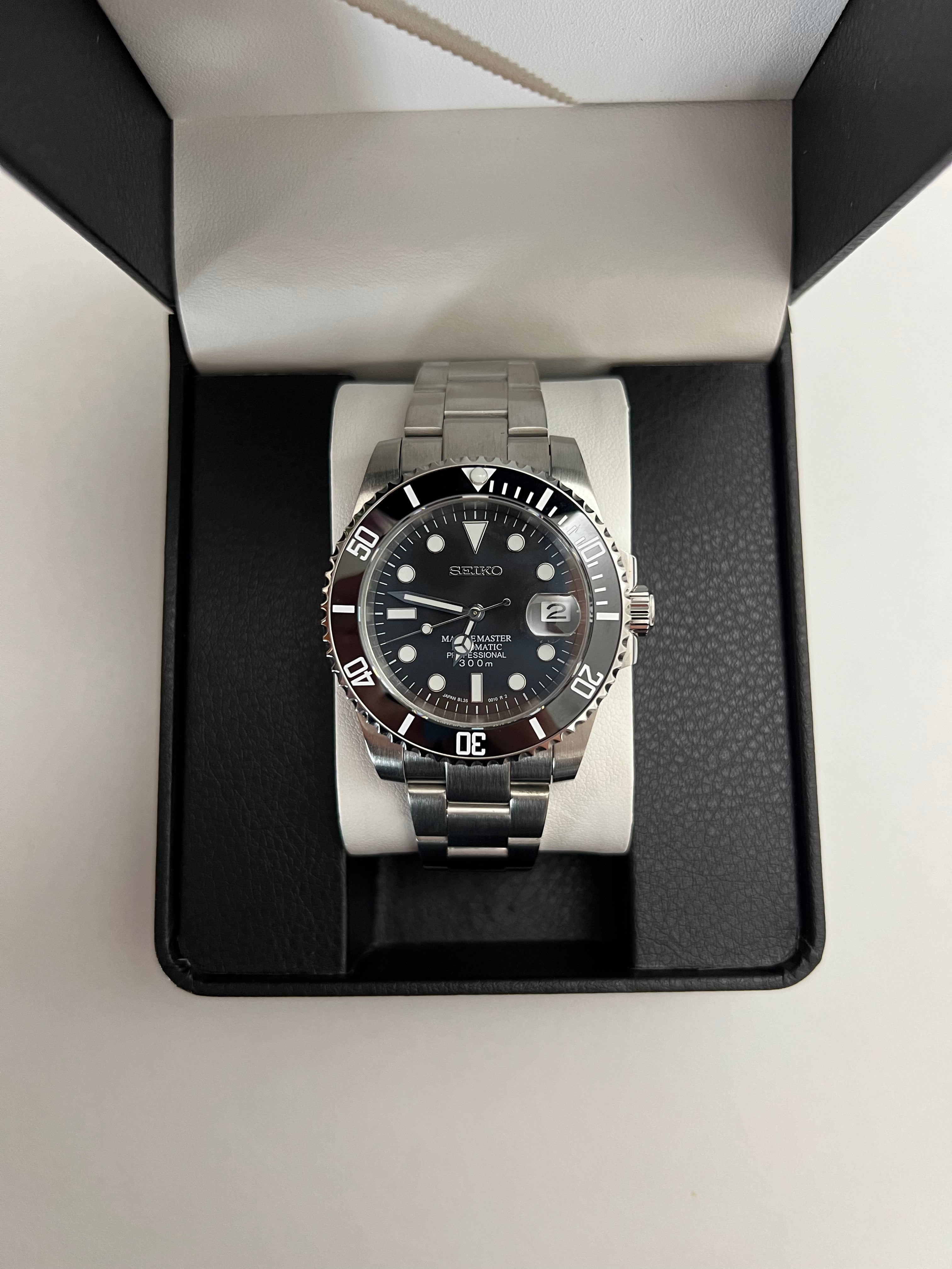Submariner (Black) Seiko NH35 automatic mod watch. A full watch with a black dial and black bezel on a metal bracelet inside an open black box.