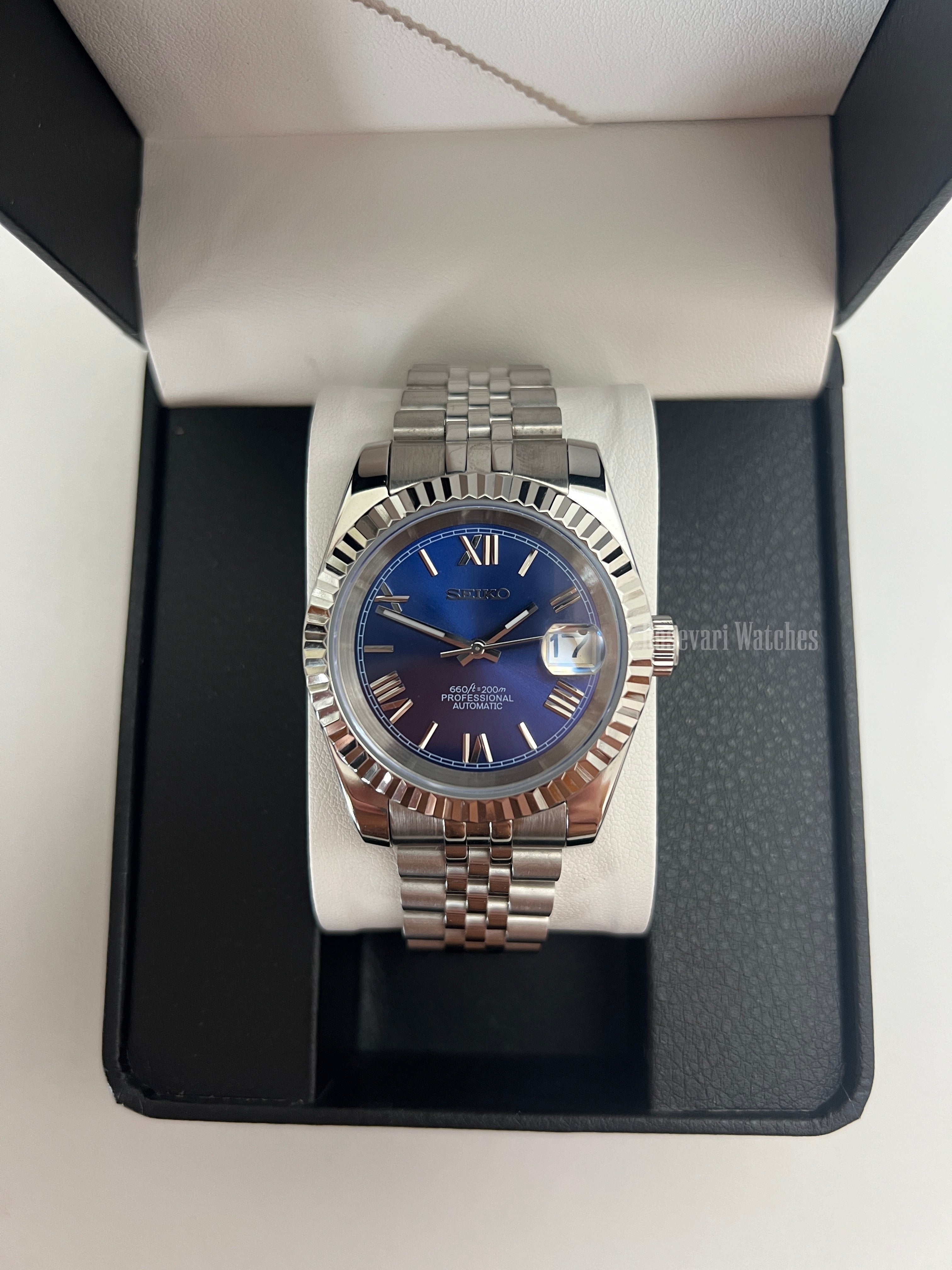 Datejust (Royal Blue Roman) Seiko NH35 automatic mod watch. A blue dial watch with a silver fluted bezel and jubilee bracelet shown in a box from a front view.