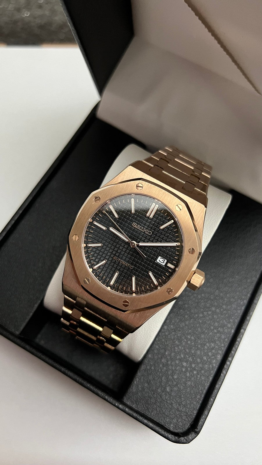 Royal Oak (Rose Gold) Seiko NH35 automatic mod watch. A slightly angled view shows the rose gold watch with a black dial inside an open black display box.