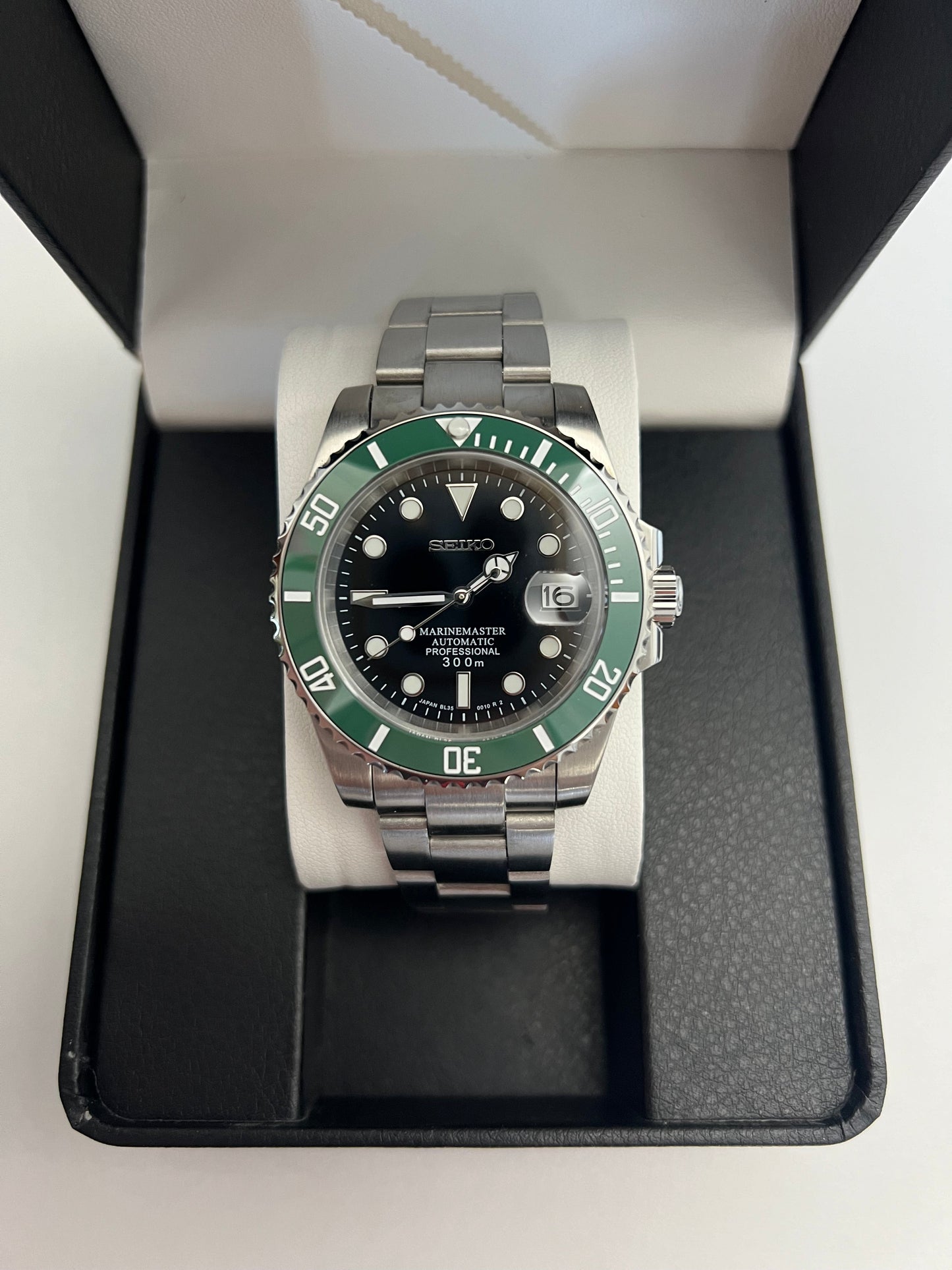Submariner (Kermit) Seiko NH35 automatic mod watch. A full watch with a black dial and green bezel on a metal link bracelet inside an open watch box.