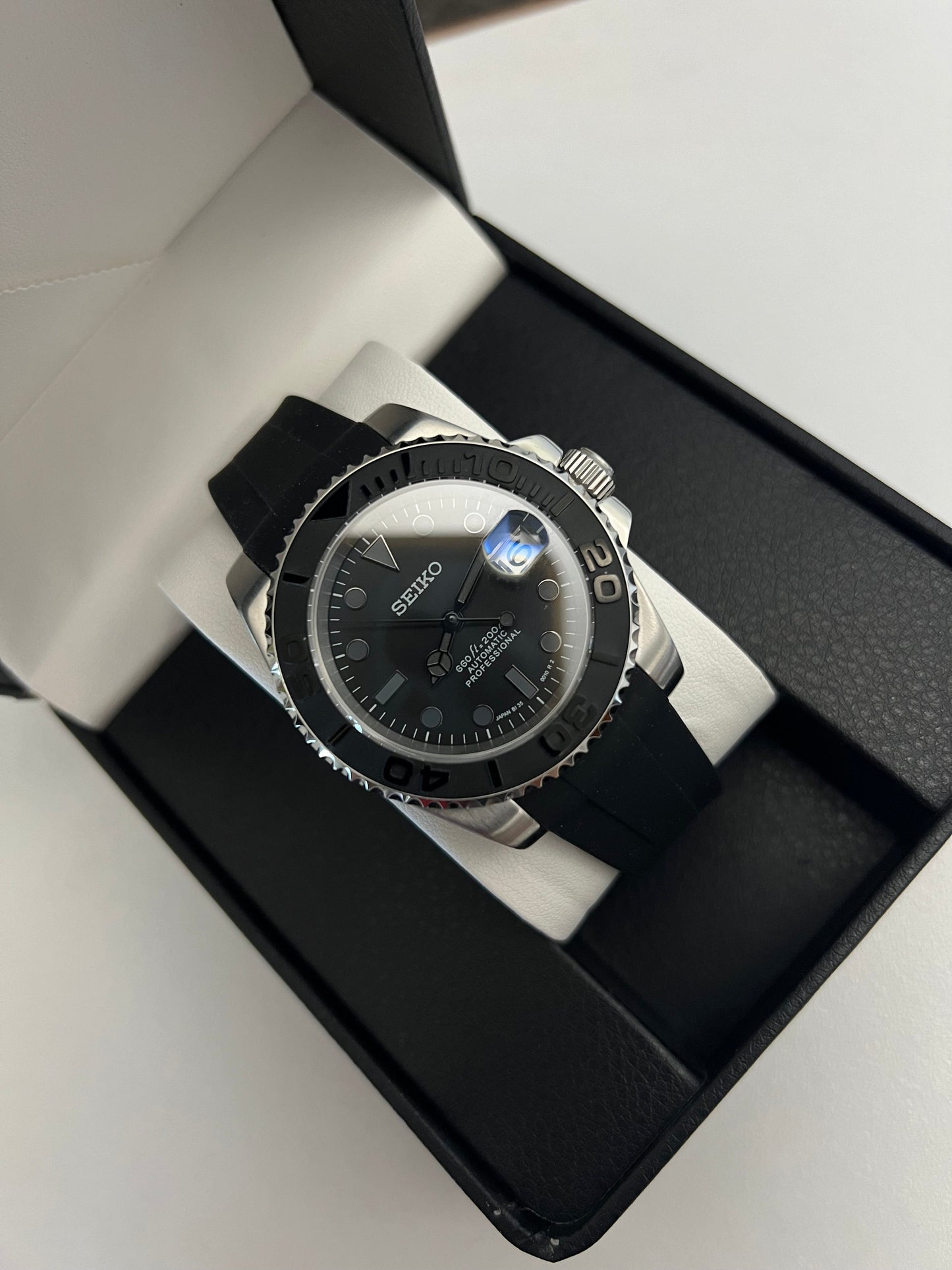 Yacht-Master (Grey) Seiko NH35 automatic mod watch. A full watch with a black dial and bezel on a black rubber strap inside a watch box.