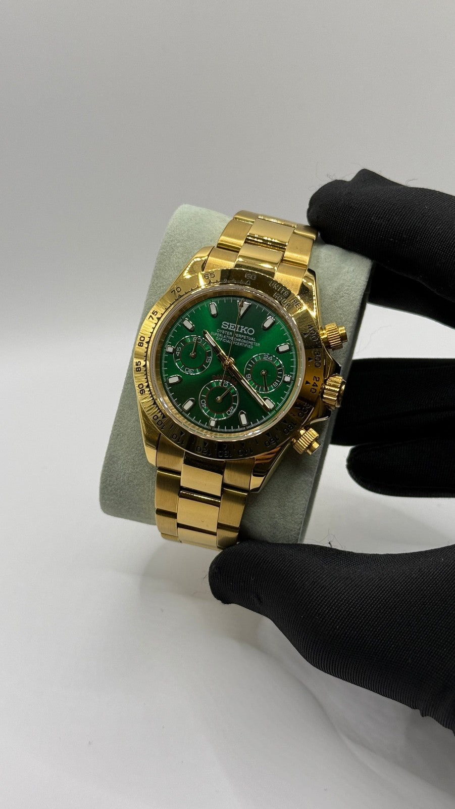 Daytona (Green & Gold) Seiko VK63 meca-quartz chronograph mod watch. A full watch shot shows a green dial with a gold bezel and a gold metal link bracelet held by a gloved hand.