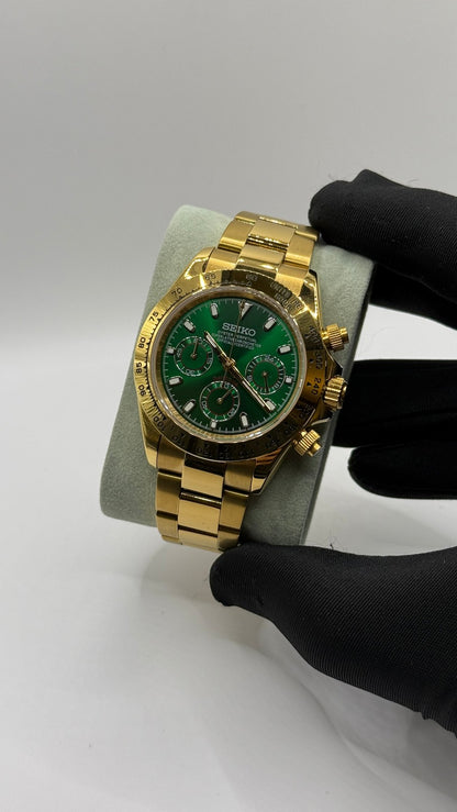 Daytona (Green & Gold) Seiko VK63 meca-quartz chronograph mod watch. A full watch shot shows a green dial with a gold bezel and a gold metal link bracelet held by a gloved hand.