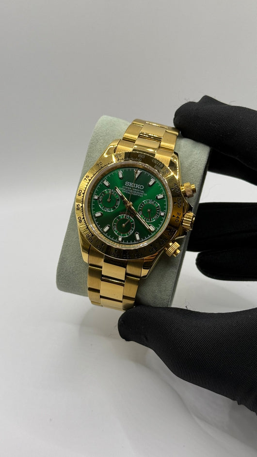 Daytona (Green & Gold) Seiko VK63 meca-quartz chronograph mod watch. A full watch shot shows a green dial with a gold bezel and a gold metal link bracelet held by a gloved hand.