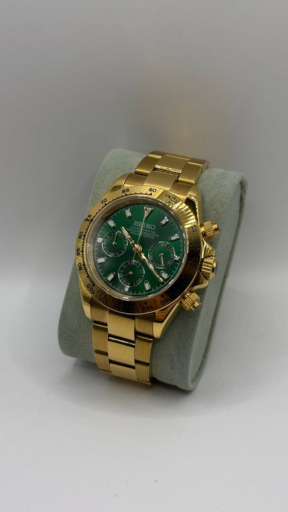 Daytona (Green & Gold) Seiko VK63 meca-quartz chronograph mod watch. A full watch shot shows a green dial with a gold bezel and a gold metal link bracelet on a display cushion.