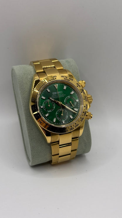 Daytona (Green & Gold) Seiko VK63 meca-quartz chronograph mod watch. A full watch shot shows a green dial with a gold bezel and a gold metal link bracelet on a display cushion.
