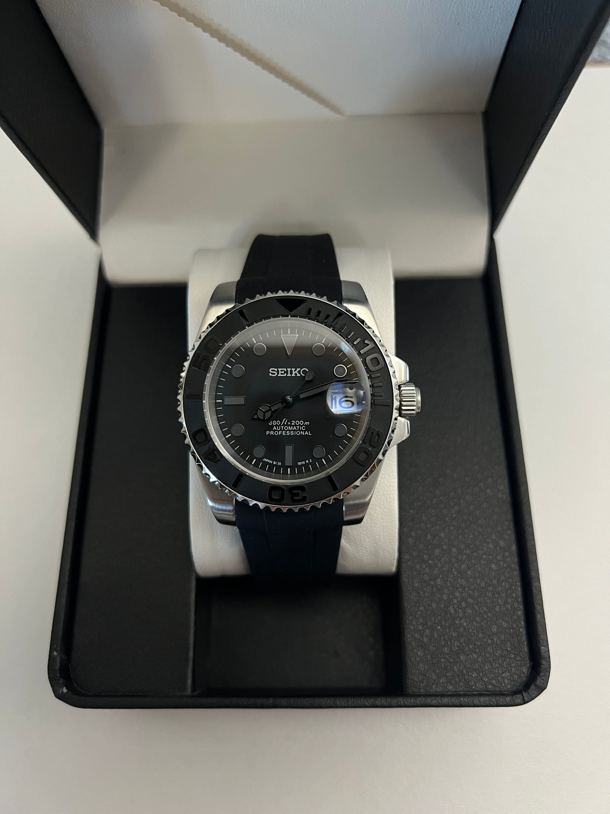 Yacht-Master (Grey) Seiko NH35 automatic mod watch. A full watch with a black dial and bezel on a black rubber strap inside a watch box.