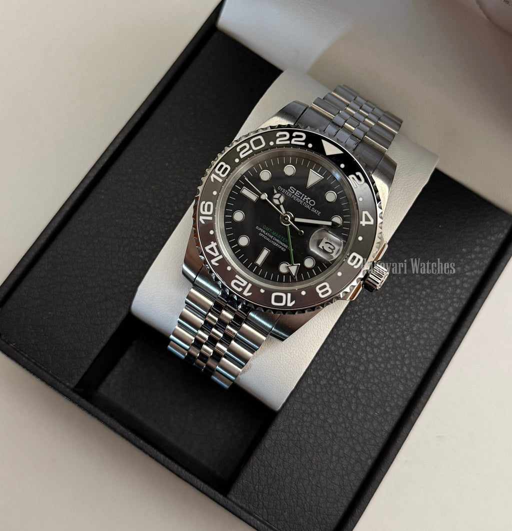 GMT (Bruce Wayne) Seiko NH34 GMT automatic mod watch. A full watch shot of a black dial watch with a black bezel inside a black presentation box.