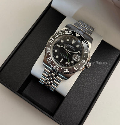 GMT (Bruce Wayne) Seiko NH34 GMT automatic mod watch. A full watch shot of a black dial watch with a grey and black bezel inside a black presentation box.