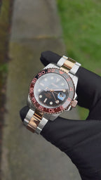 GMT (Rootbeer) Seiko NH34 GMT automatic mod watch. A full watch with a black dial and a black and rose gold bezel on a two tone oyster bracelet held in a glove.