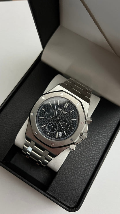 Royal Oak Chrono (Black) Seiko VK63 meca-quartz chronograph mod watch. A slightly angled shot of a silver chronograph watch with a black textured dial in a black display box.