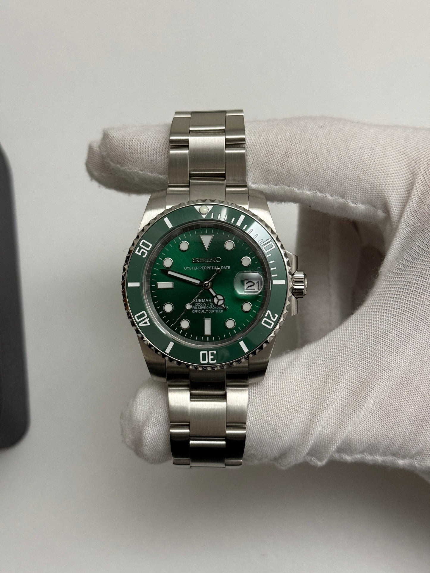 Submariner (Hulk) Seiko NH35 automatic mod watch. A full watch shot shows a green dial and green bezel on a silver metal link bracelet held by a gloved hand.
