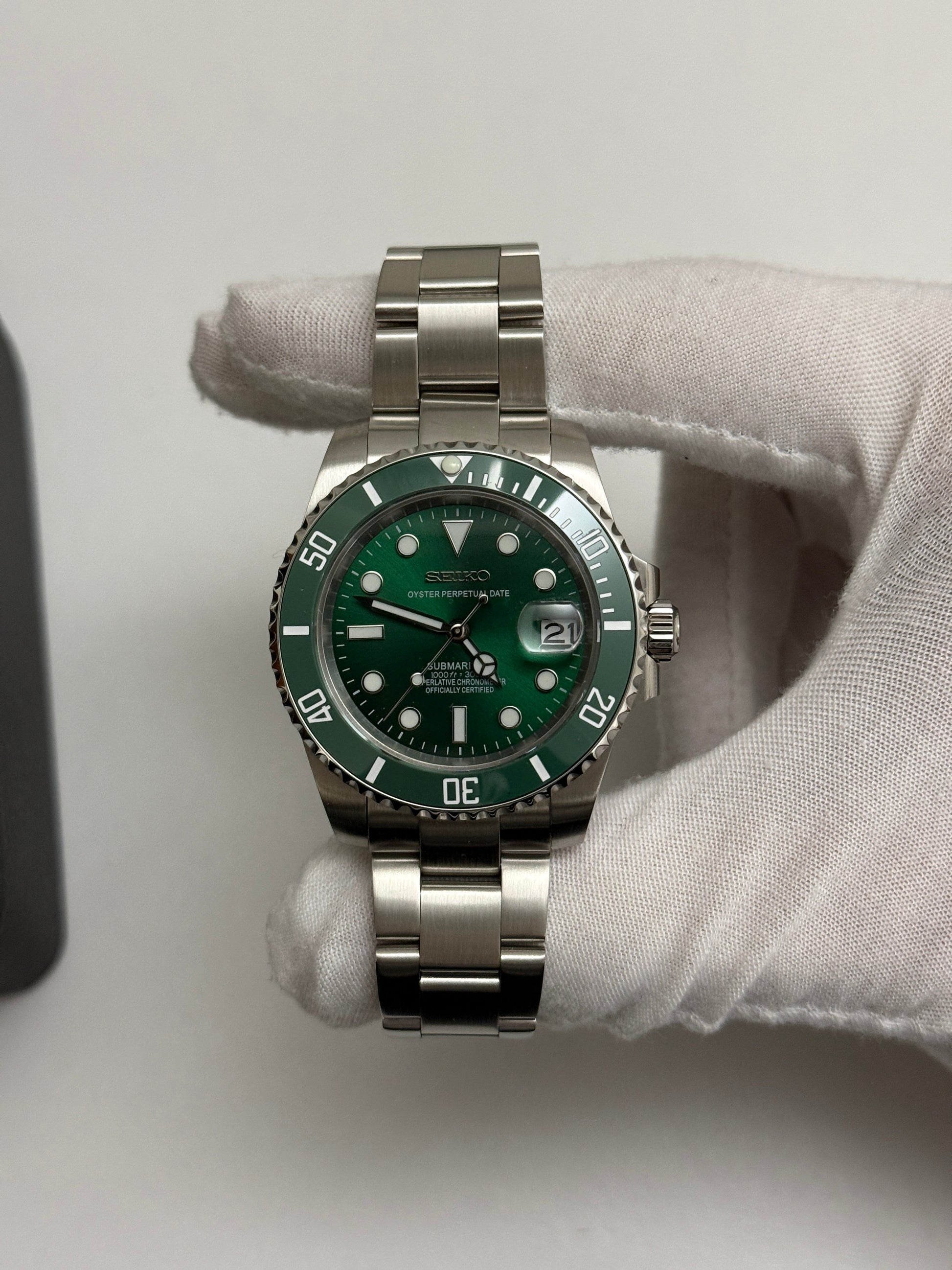 Submariner (Hulk) Seiko NH35 automatic mod watch. A full watch shot shows a green dial and green bezel on a silver metal link bracelet held by a gloved hand.