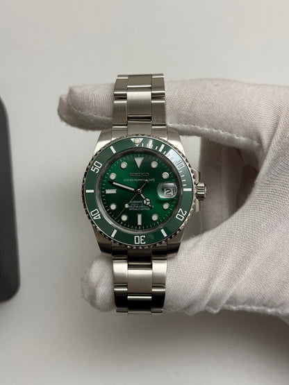 Submariner (Hulk) Seiko NH35 automatic mod watch. A full watch shot shows a green dial and green bezel on a silver metal link bracelet held by a gloved hand.