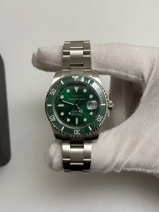 Submariner (Hulk) Seiko NH35 automatic mod watch. A full watch shot shows a green dial and green bezel on a silver metal link bracelet held by a gloved hand.