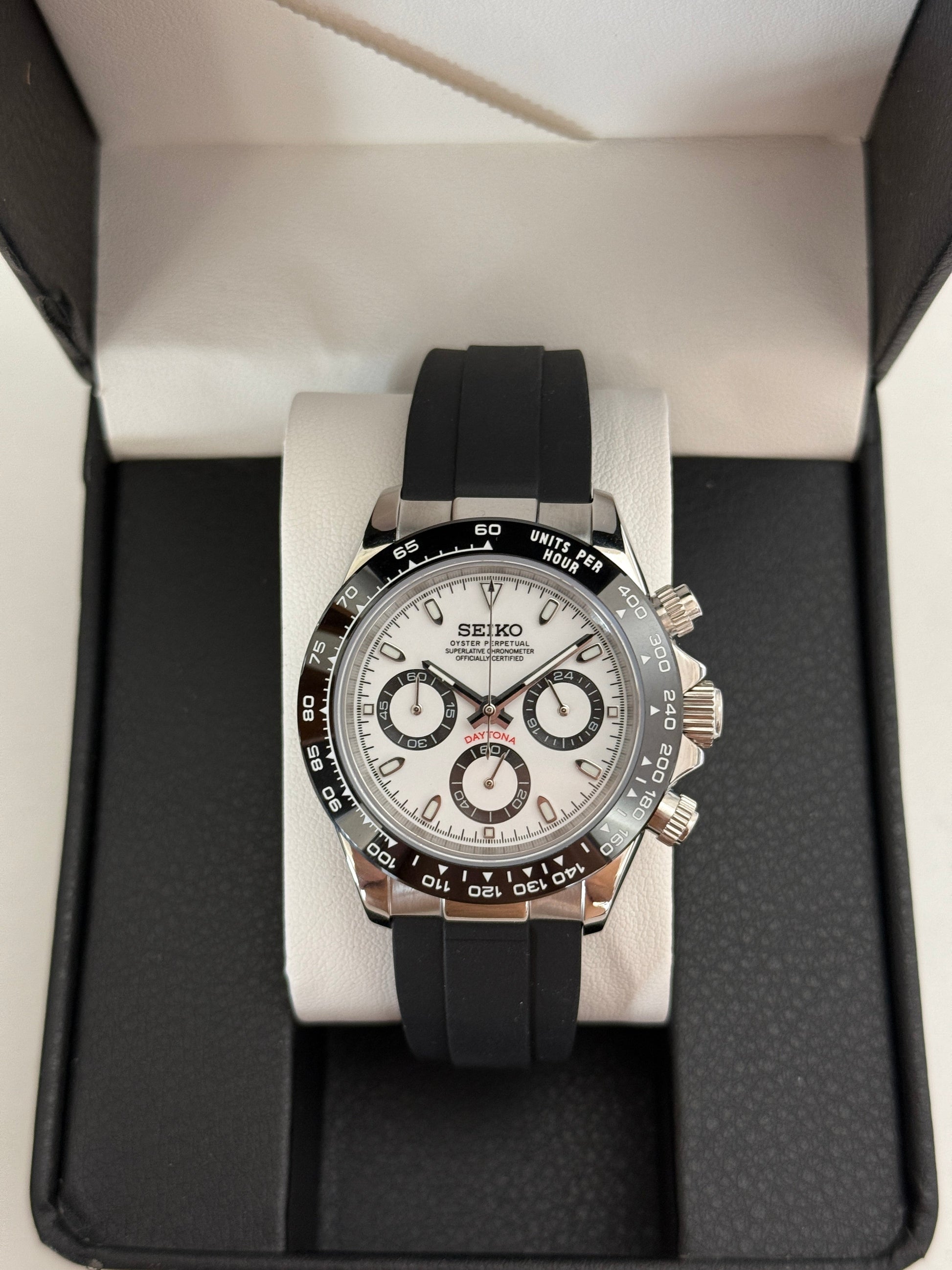 Daytona (Panda) Seiko VK63 meca-quartz chronograph mod watch. A full watch shot in a box showing a white dial with black sub dials and a black bezel on a rubber strap.