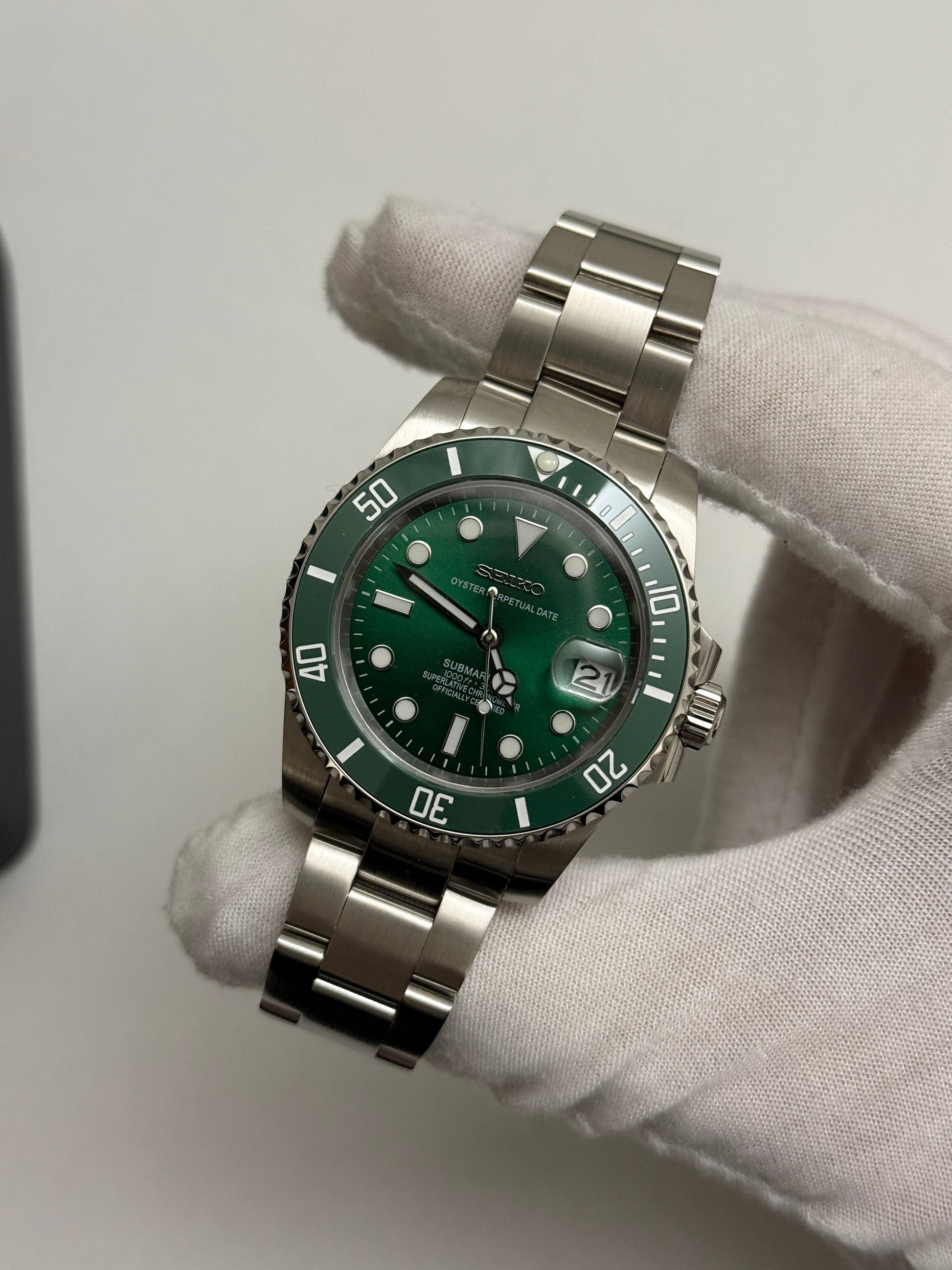 Submariner (Hulk) Seiko NH35 automatic mod watch. A full watch shot shows a green dial and green bezel on a silver metal link bracelet held by a gloved hand.