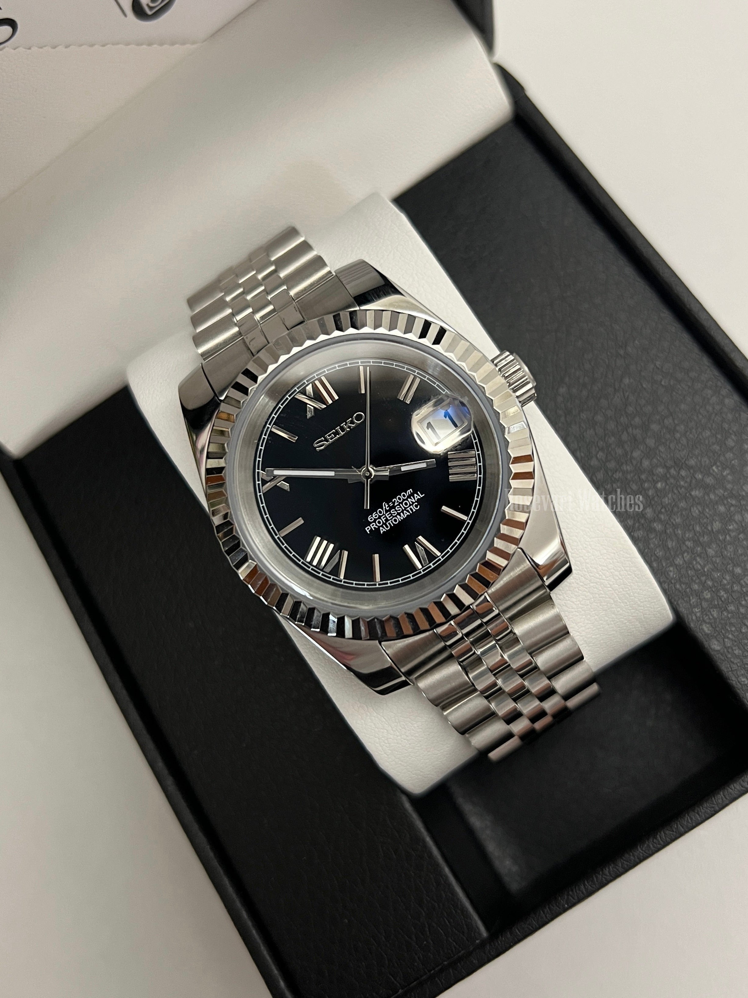 Datejust (Black Roman) Seiko NH35 automatic mod watch. A black dial watch with a silver fluted bezel and jubilee bracelet inside a box in a high angle shot.
