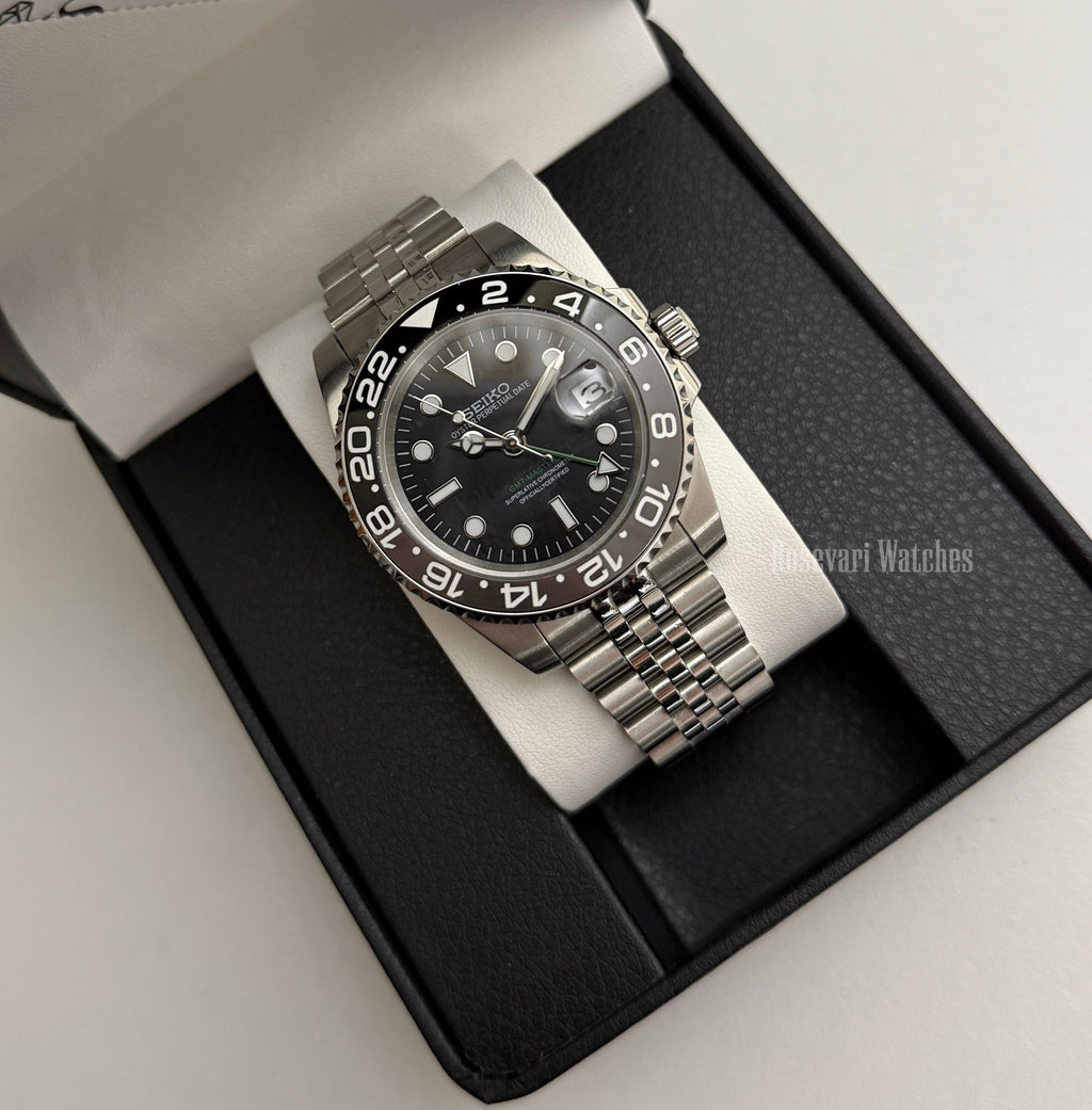 GMT (Bruce Wayne) Seiko NH34 GMT automatic mod watch. A full watch shot of a black dial watch with a black bezel inside a black presentation box.