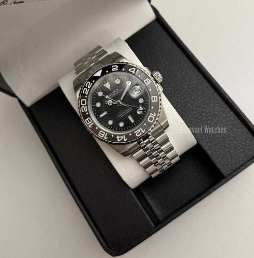 GMT (Bruce Wayne) Seiko NH34 GMT automatic mod watch. A full watch shot of a black dial watch with a black bezel inside a black presentation box.