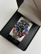 GMT (Pepsi) Seiko NH34 GMT automatic mod watch. A full watch shot inside a box shows a black dial with a blue and red bezel on a silver jubilee bracelet.