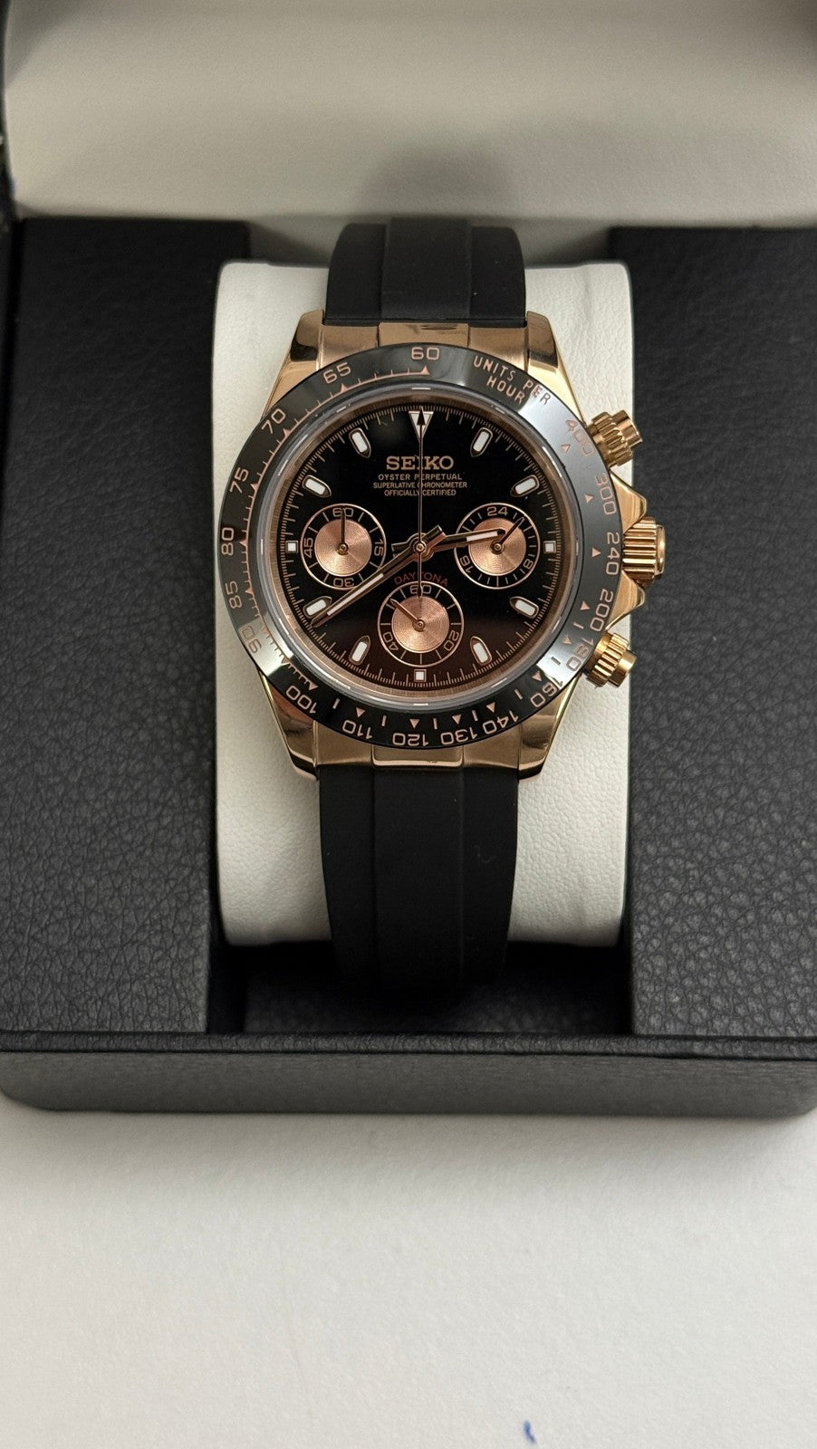 Daytona (Black & Rose Gold) Seiko VK63 meca-quartz chronograph mod watch. A black dial watch with a black bezel and black rubber strap shown in a full watch box shot.