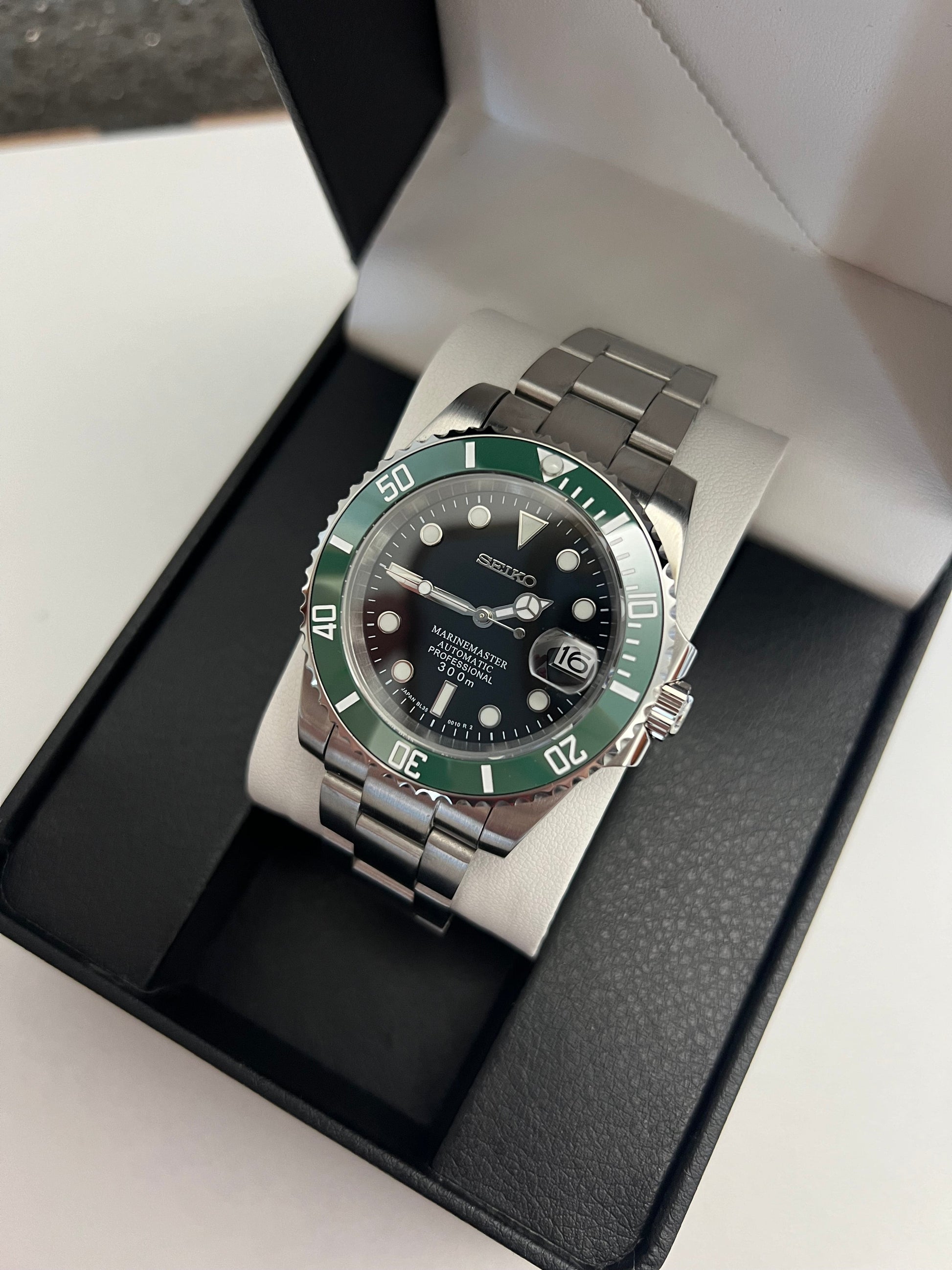 Submariner (Kermit) Seiko NH35 automatic mod watch. A full watch with a black dial and green bezel on a metal link bracelet inside an open watch box.