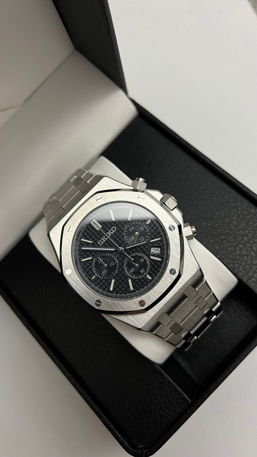 Royal Oak Chrono (Black) Seiko VK63 meca-quartz chronograph mod watch. A high angle shot of a silver chronograph watch with a black textured dial in a black display box.
