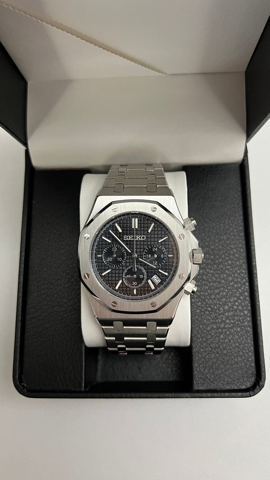 Royal Oak Chrono (Black) Seiko VK63 meca-quartz chronograph mod watch. A top down shot of a silver chronograph watch with a black textured dial in a black display box.