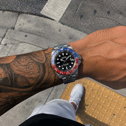 GMT (Pepsi) Seiko NH34 GMT automatic mod watch. A wrist shot shows a black dial watch with a blue and red bezel on a silver jubilee bracelet.