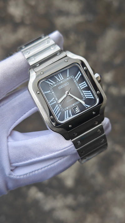 Santos (Graphite) Seiko NH35 automatic mod watch. A full watch shot held by a gloved hand showing a grey dial with a black bezel and a metal link bracelet.
